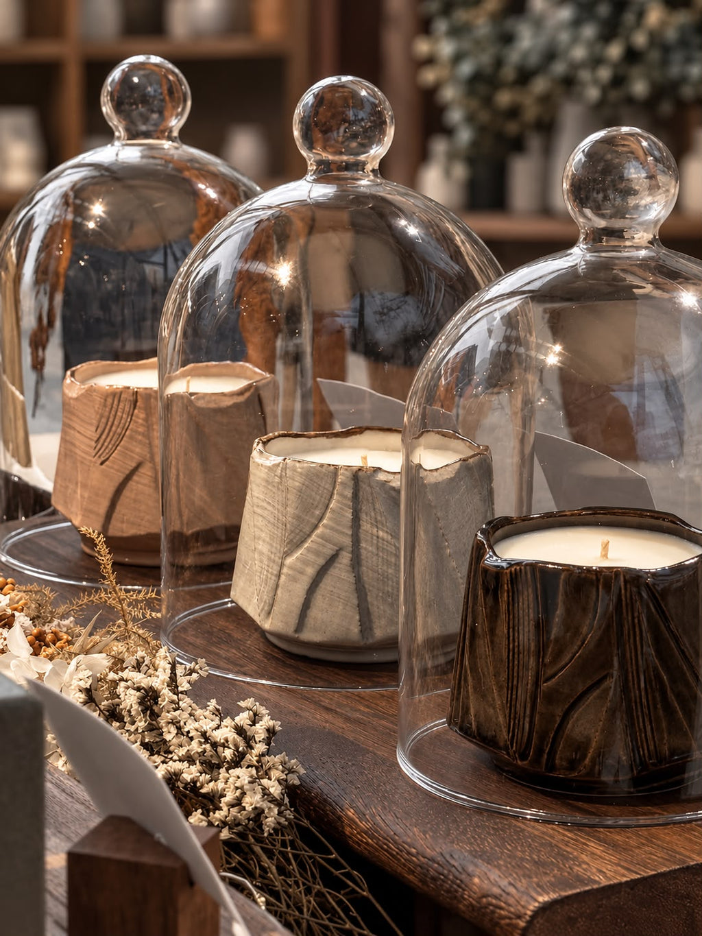 Three Mittsu Doru ceramic candles under glass domes on a wooden table